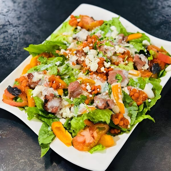 A vibrant Afghan salad with lettuce, tomatoes, peppers, meat, and a creamy dressing on a white plate.
