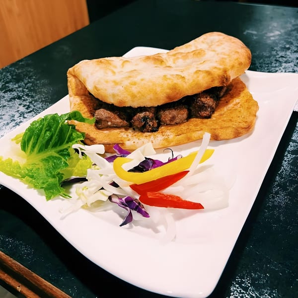 Emran Restaurant's Afghan flatbread sandwich with meat, lettuce, and colorful bell peppers on a white plate.