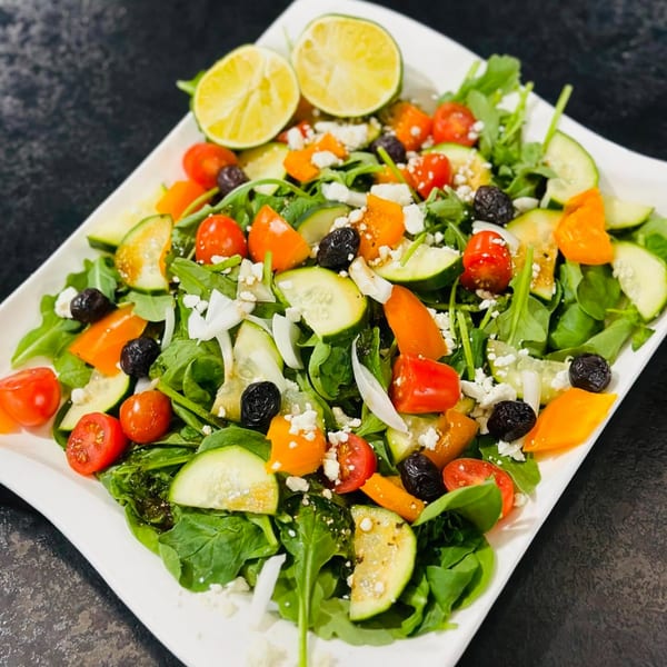 A vibrant Afghan salad with greens, tomatoes, cucumbers, olives, feta, and lime wedges.