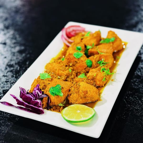 Emran Restaurant's Afghan chicken curry with cilantro, red onion, and lime on a white platter.