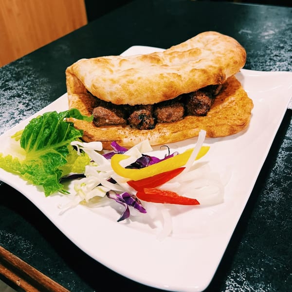 Afghan flatbread sandwich with meat and a side of fresh salad on a white plate.